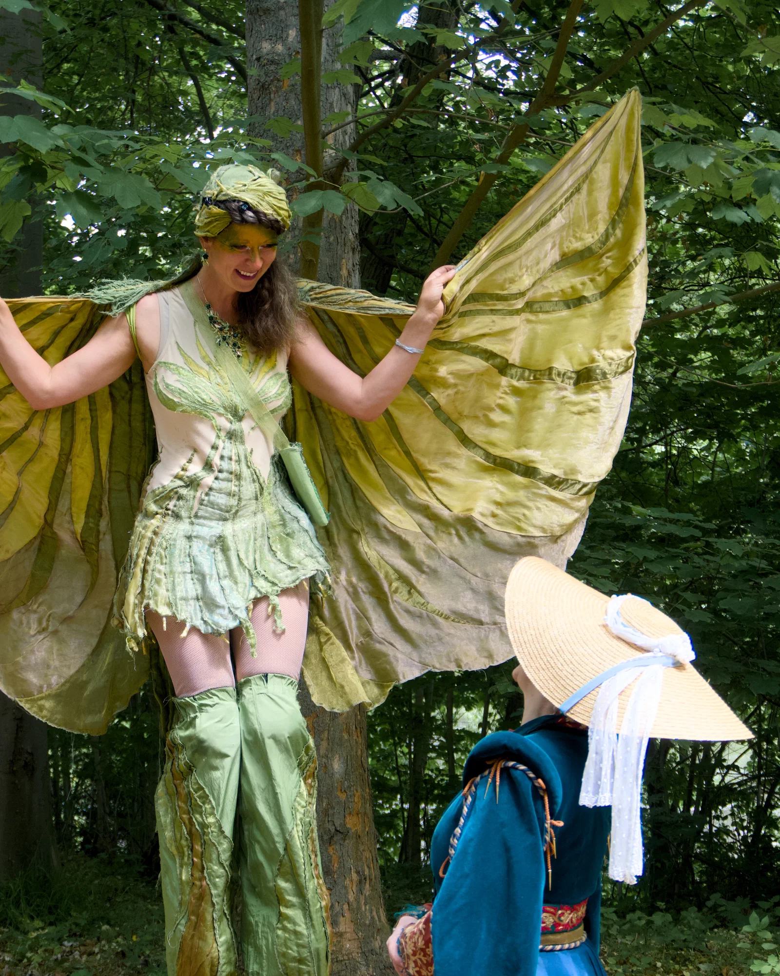 A performer on stilts in a green fairy costume