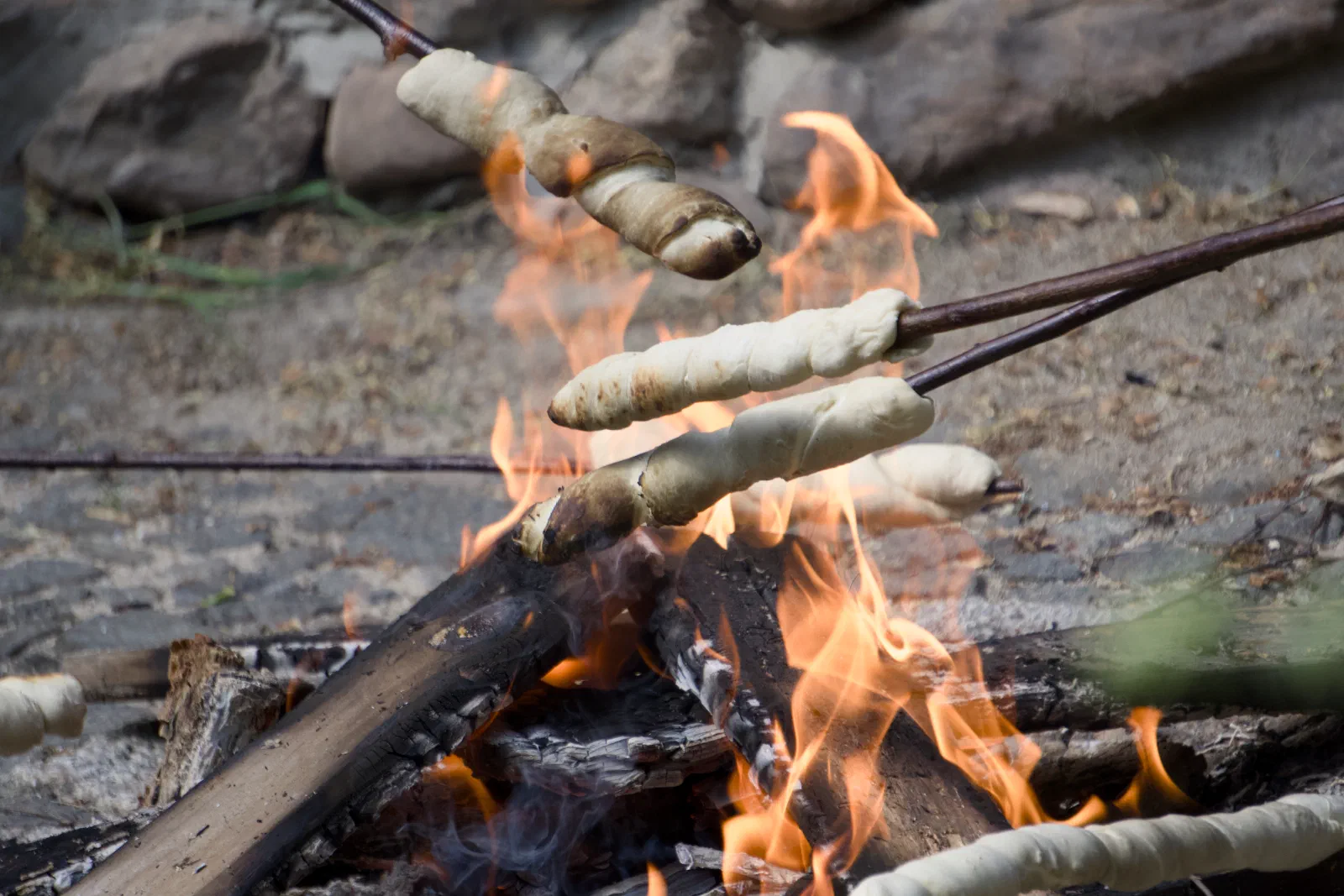 Dough wrapped on sticks baking over the flames of a campfire