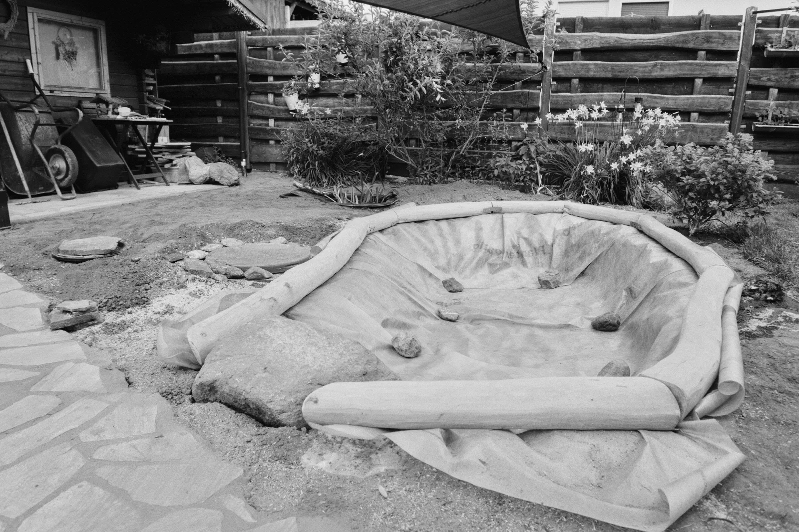 Black and white photo of a dug-out sandpit edged with logs and lined ready for sand