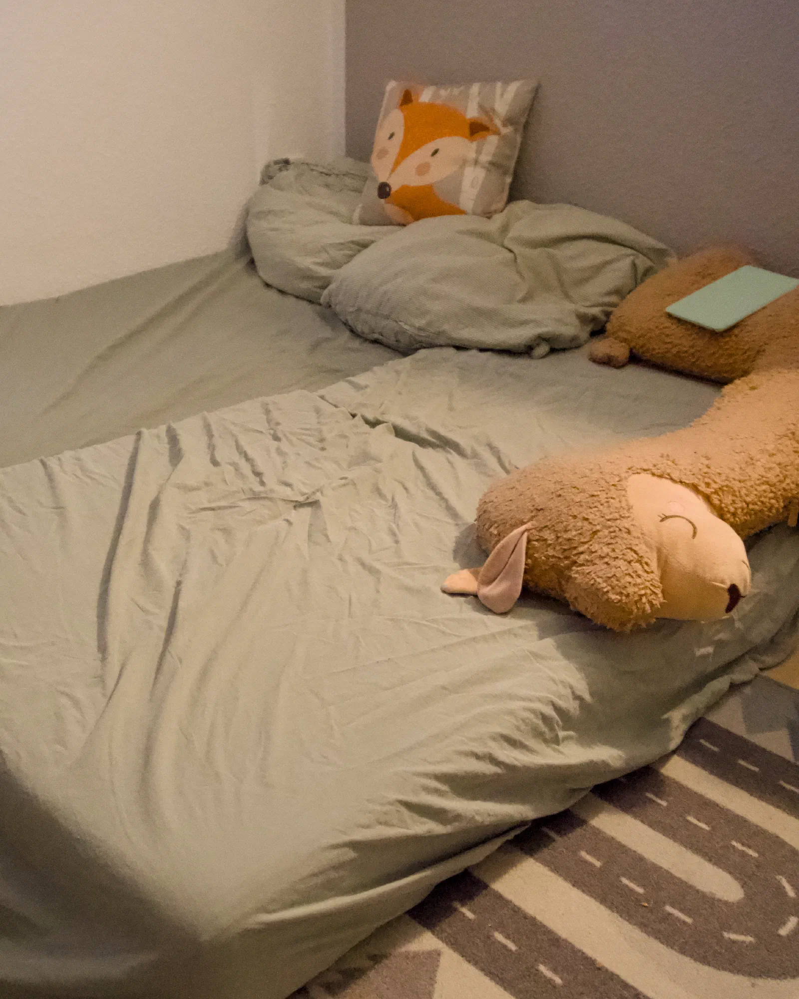 Makeshift floor bed in the playroom with a fox cushion and a sheep plush