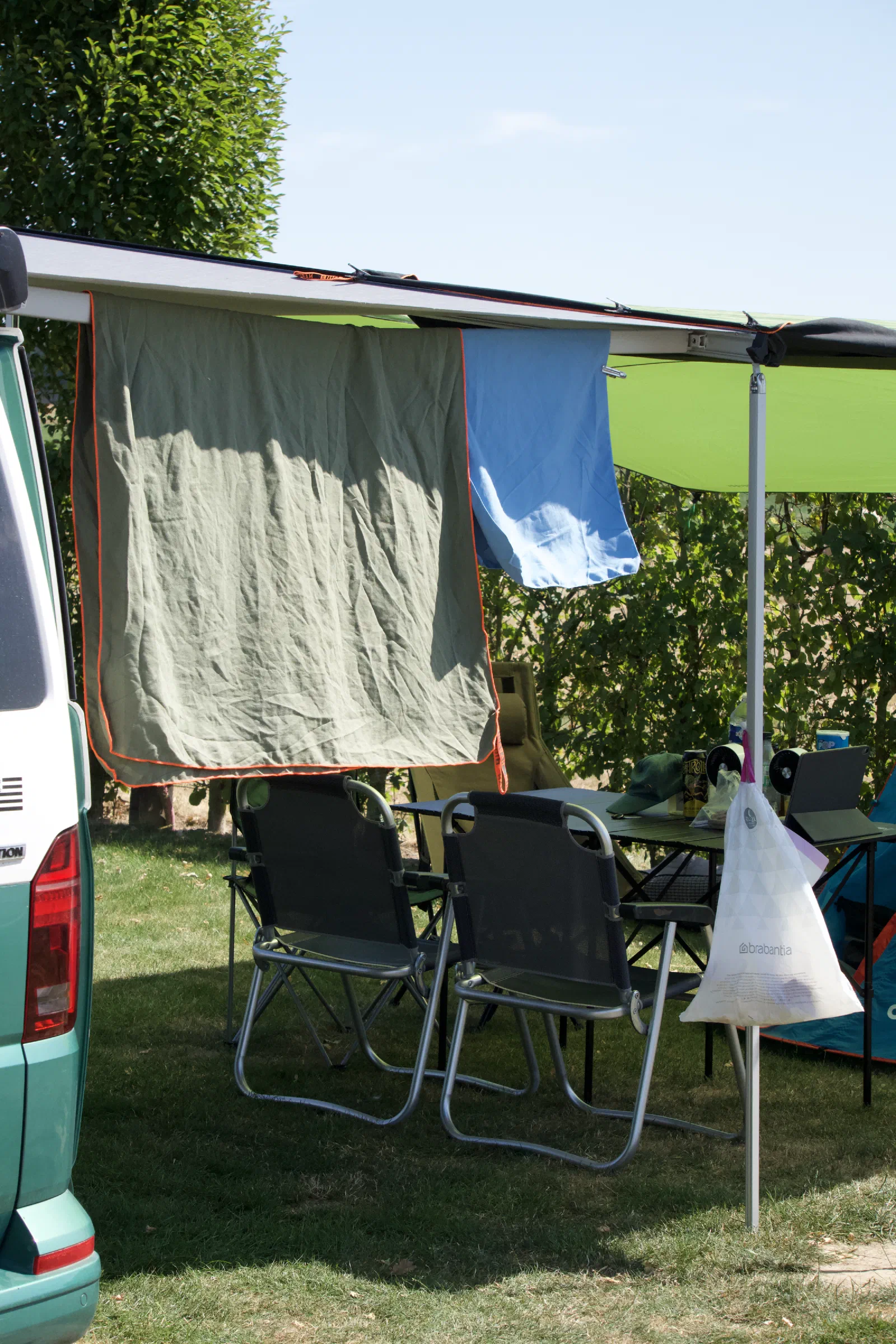 California with the awning out on a hedged pitch, towels drying