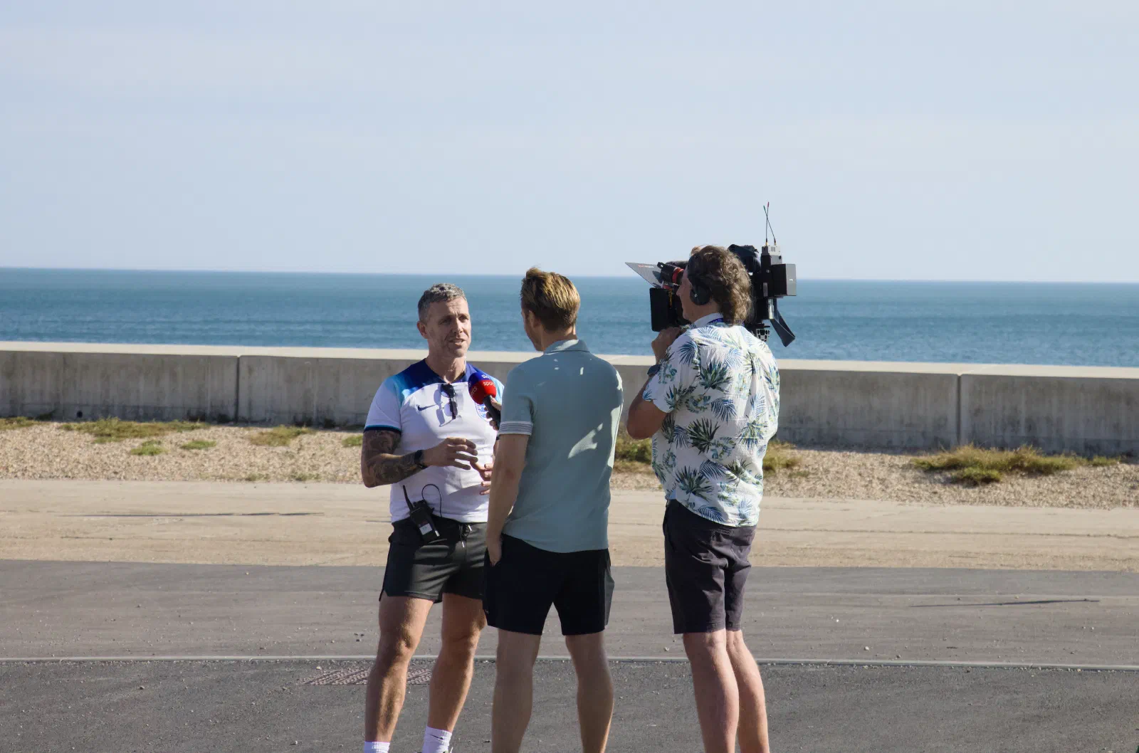 TV crew interviewing a man in an England shirt on the seafront