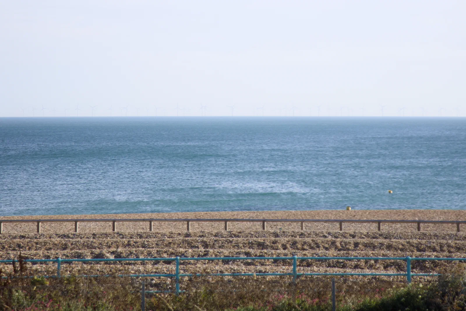 Offshore wind turbines on the horizon behind the shingle beach