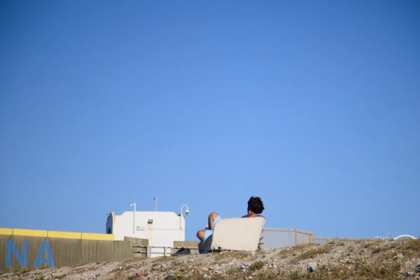 Man relaxing in an armchair on the shingle bank above the marina