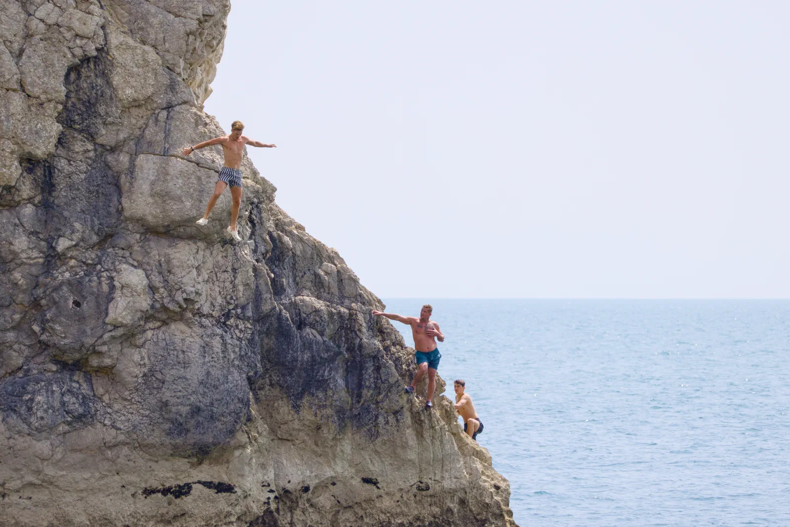 Three men climbing the rocks by the sea