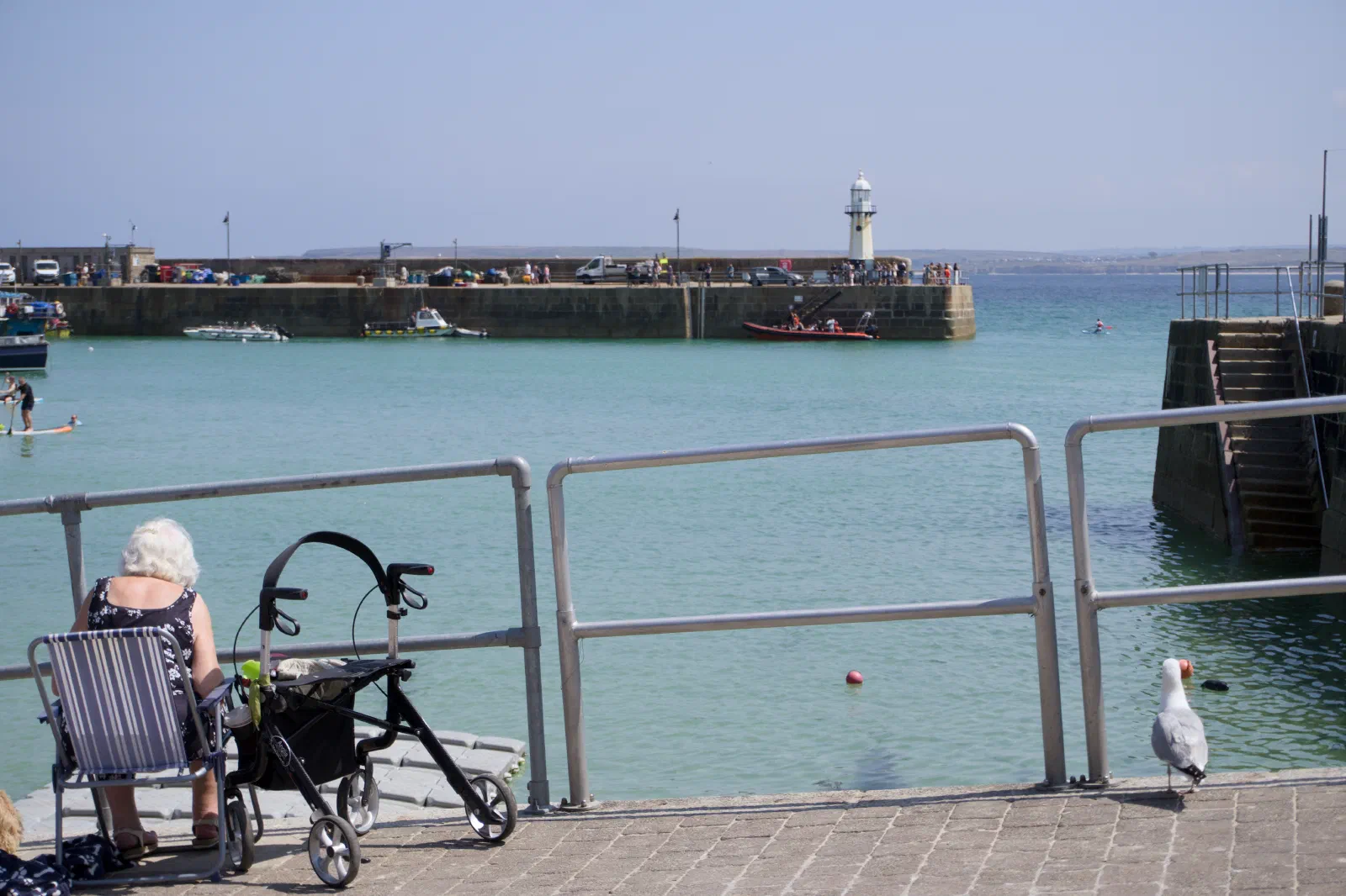 Woman with a rollator sitting at the harbour wall, the pier and lighthouse behind