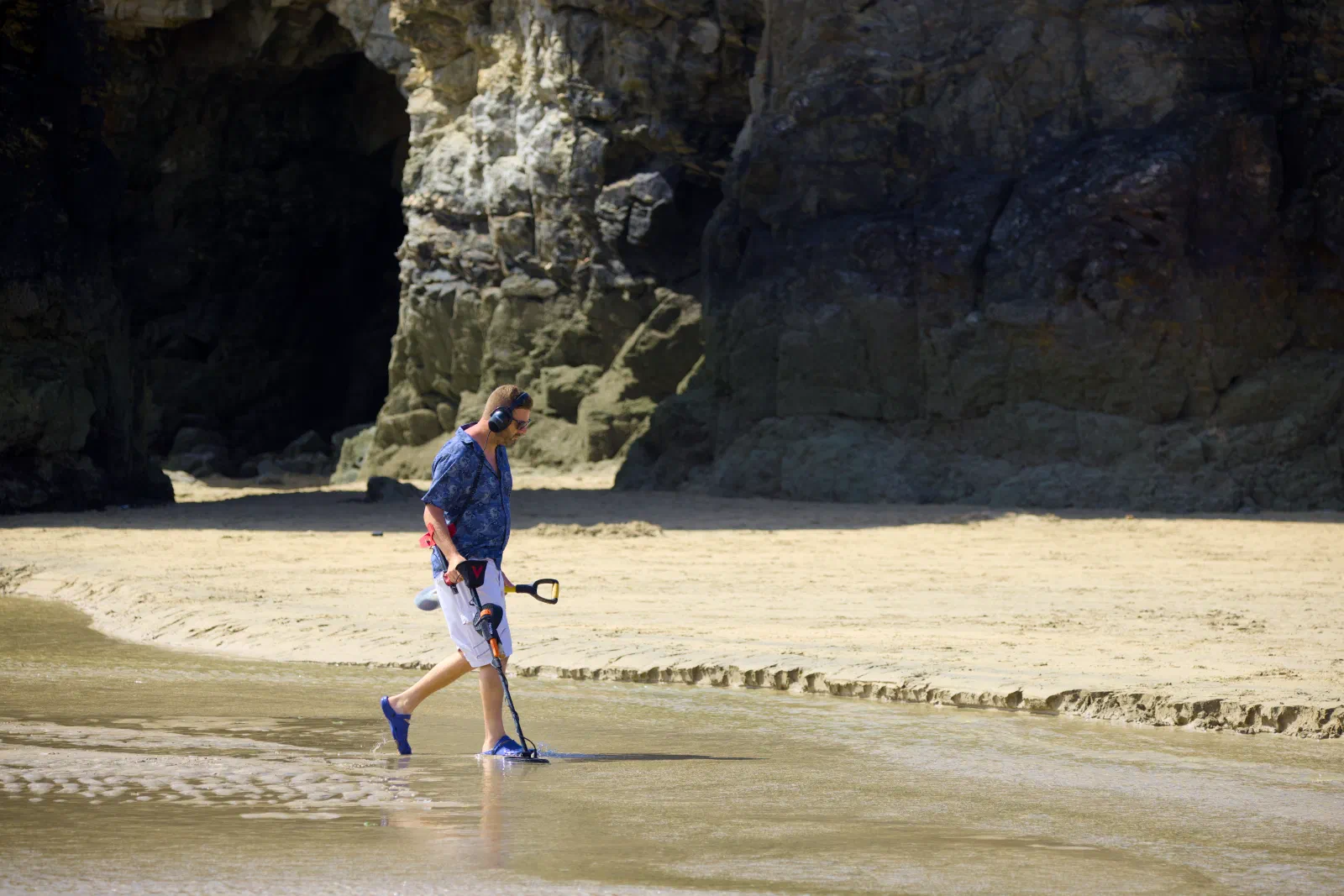 Man sweeping the wet sand with a metal detector in front of the cliffs