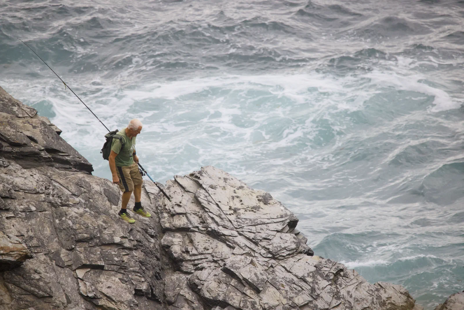 Angler with a fishing rod on the rocks above the sea