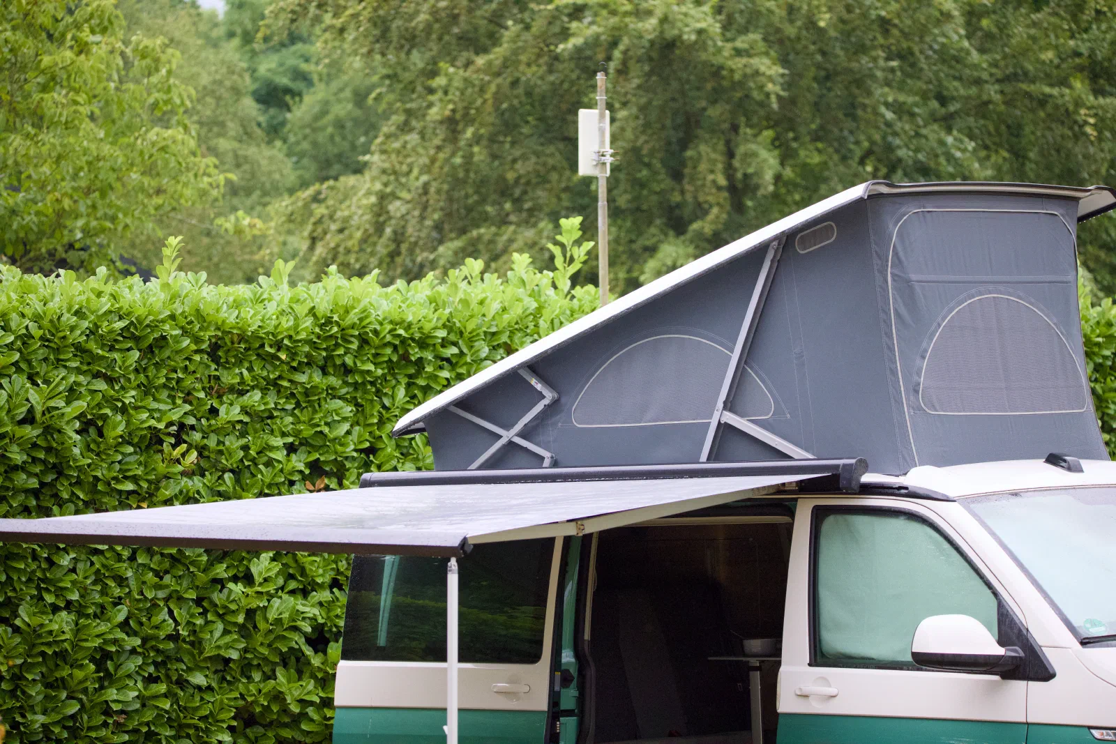 The California with the roof up and awning out next to a laurel hedge