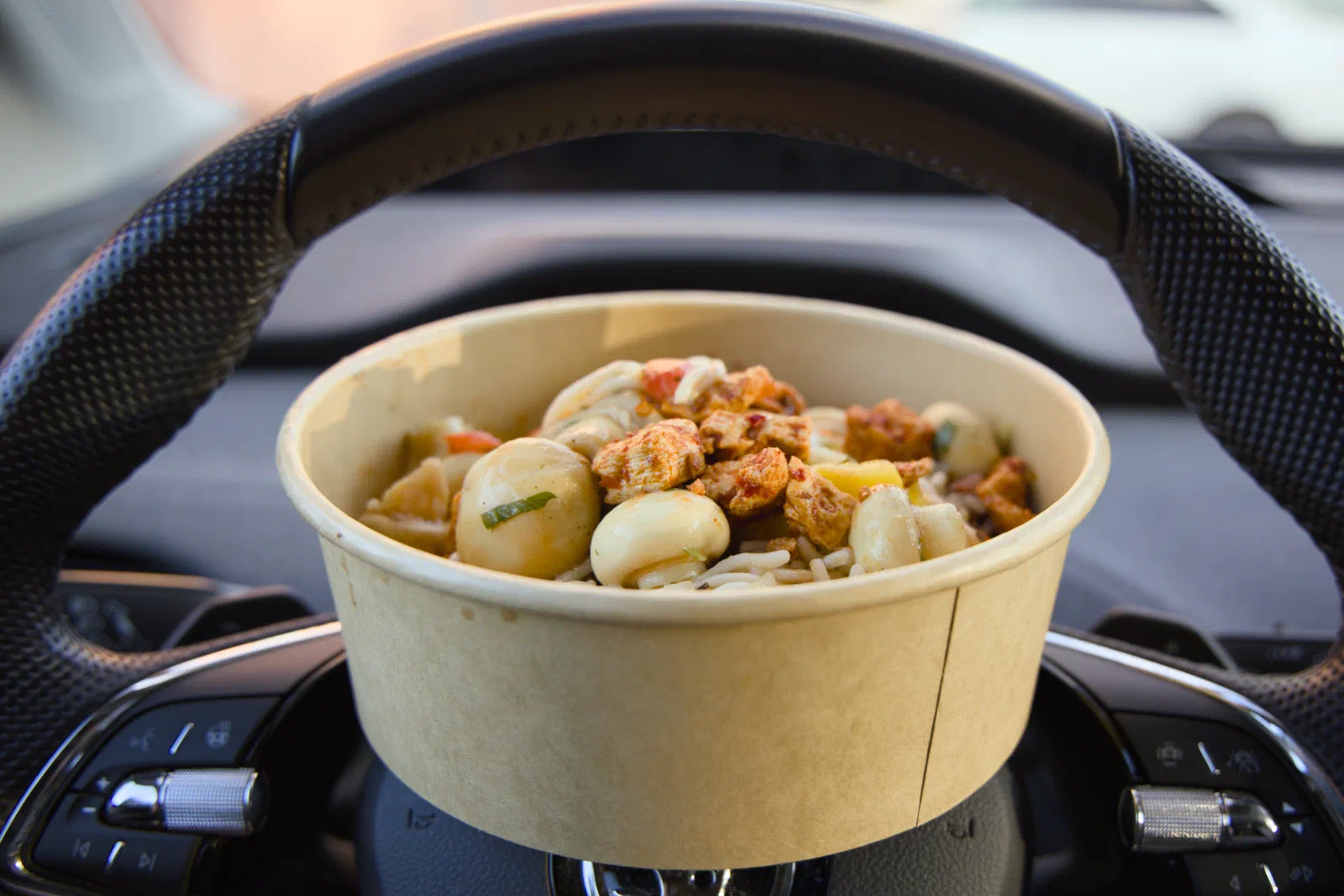 Takeaway bowl balanced on a car steering wheel