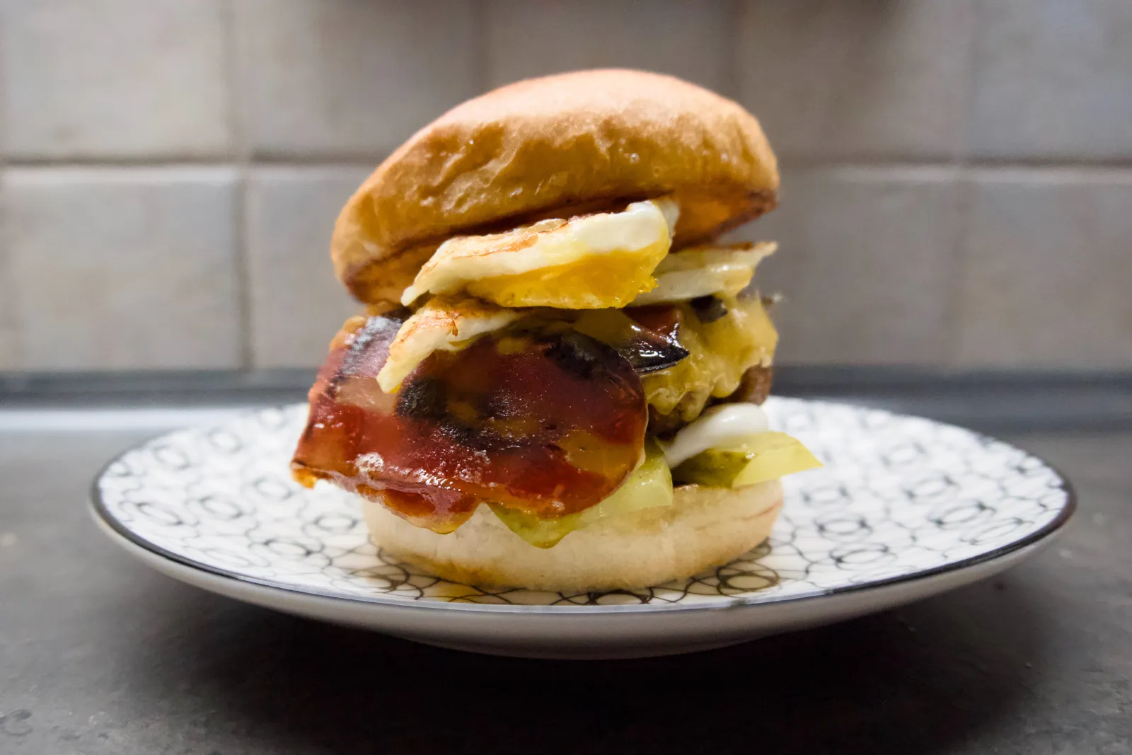 Burger with plant-based patty, fried egg, cheese, vegan bacon and pickles on a plate