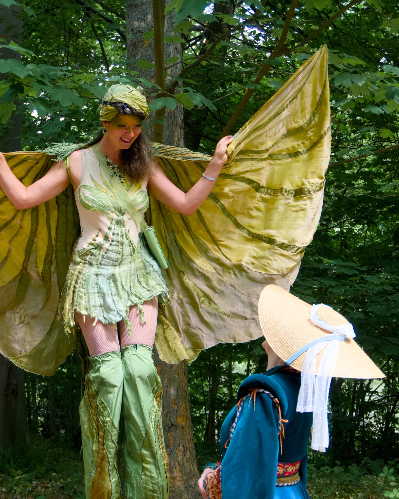 A performer on stilts in a green fairy costume
