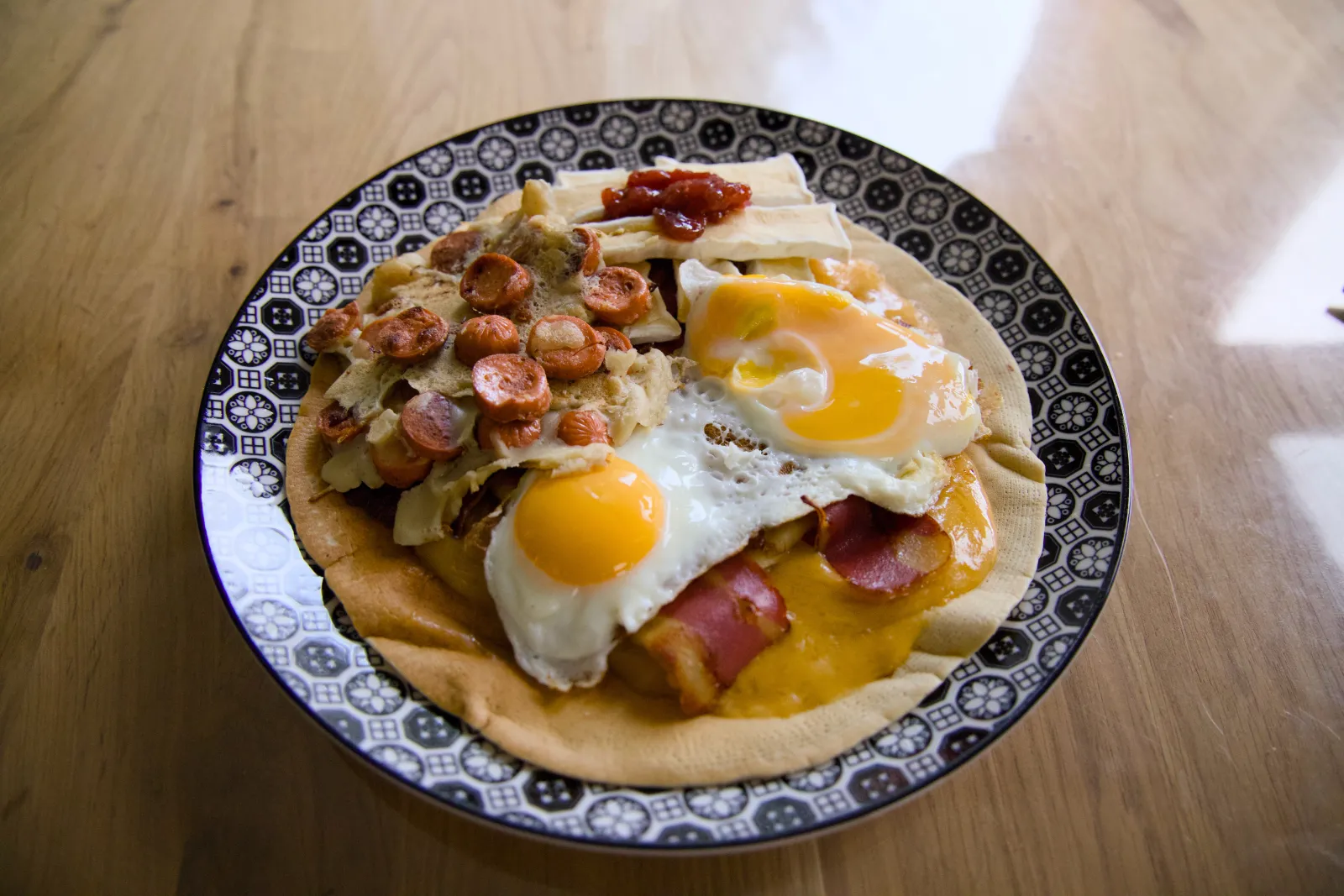 Double-layer pancake with fried eggs, vegan bacon, vegan sausage slices and strawberry jam