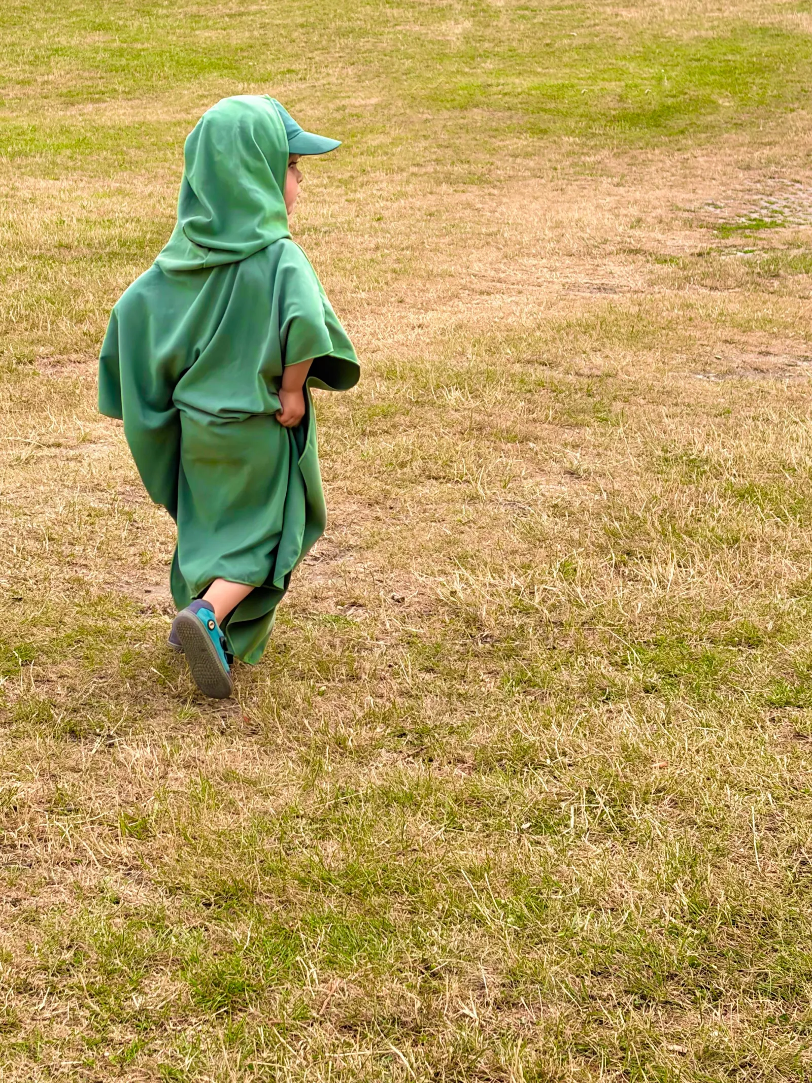 Child wrapped in a green hooded towel walking across grass