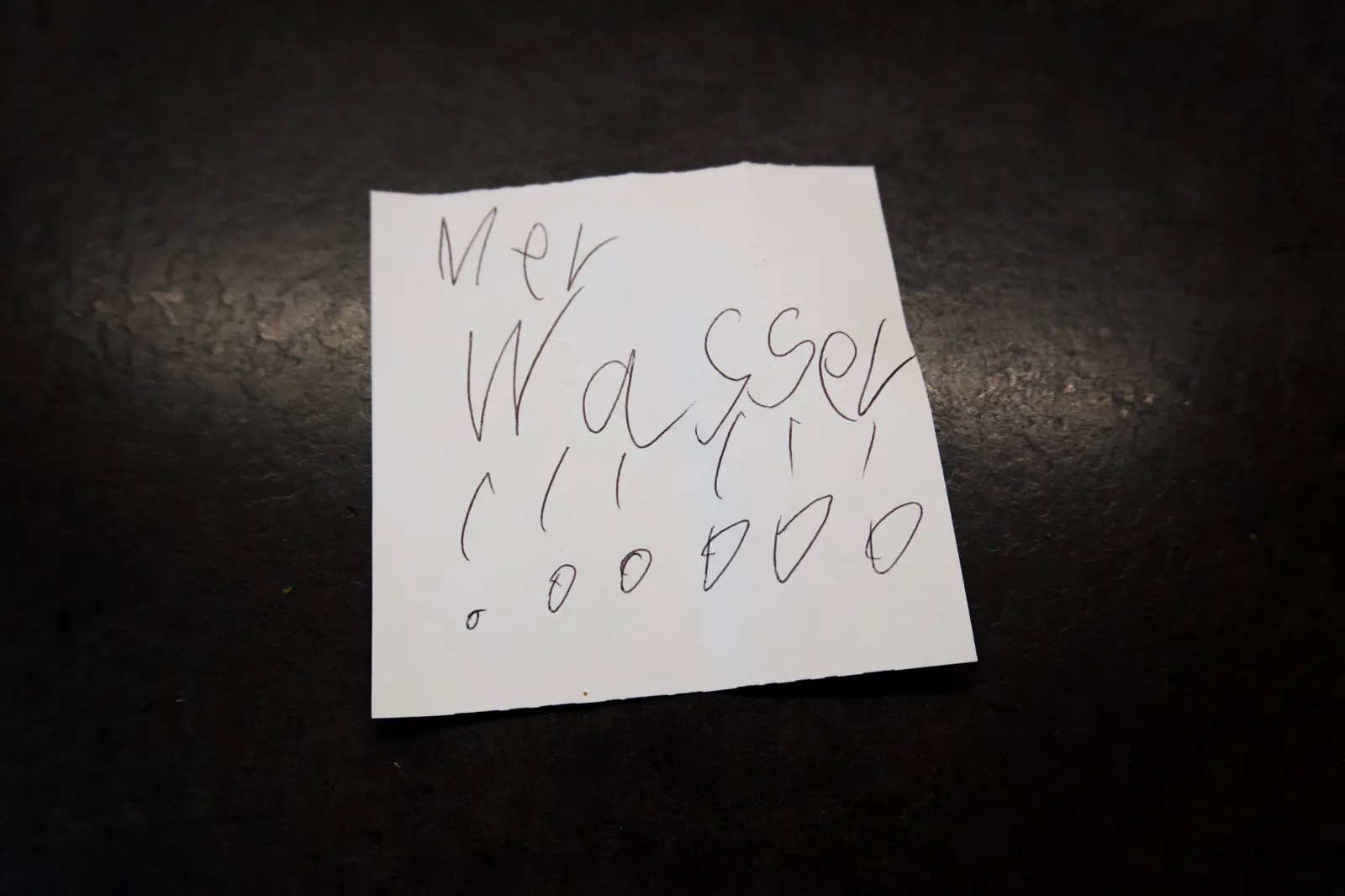 A small handwritten note on a dark surface reading 'Mer Wasser !!!' in a child's handwriting