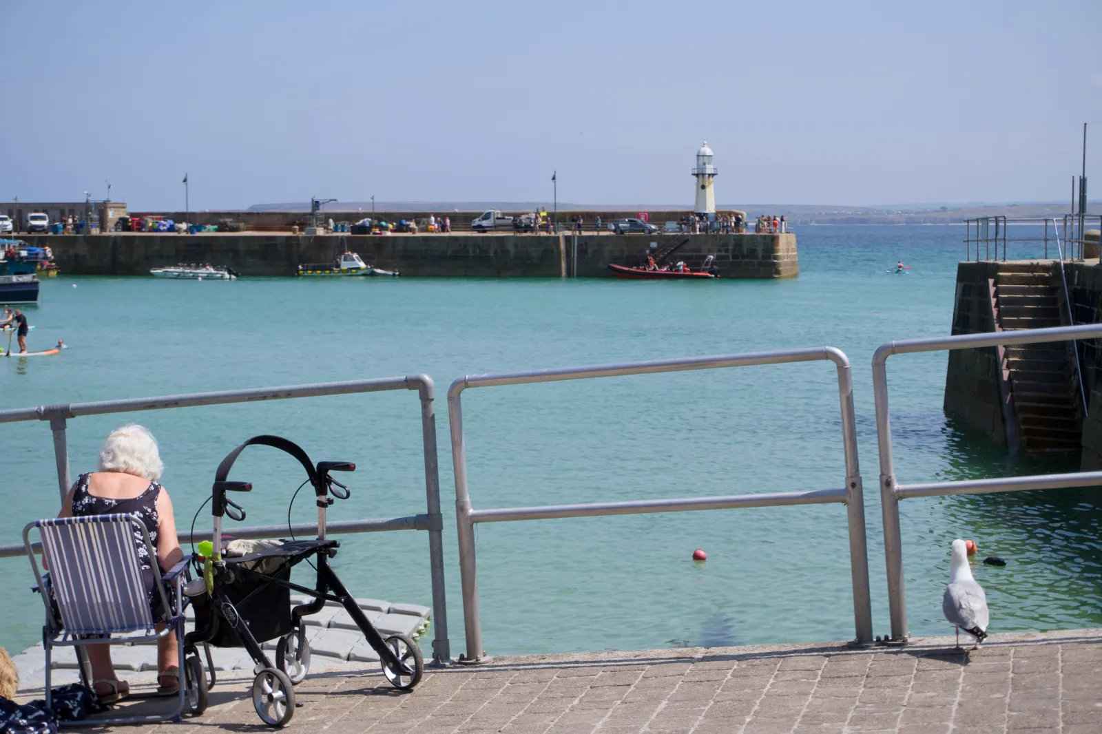 Woman with a rollator sitting at the harbour wall, the pier and lighthouse behind