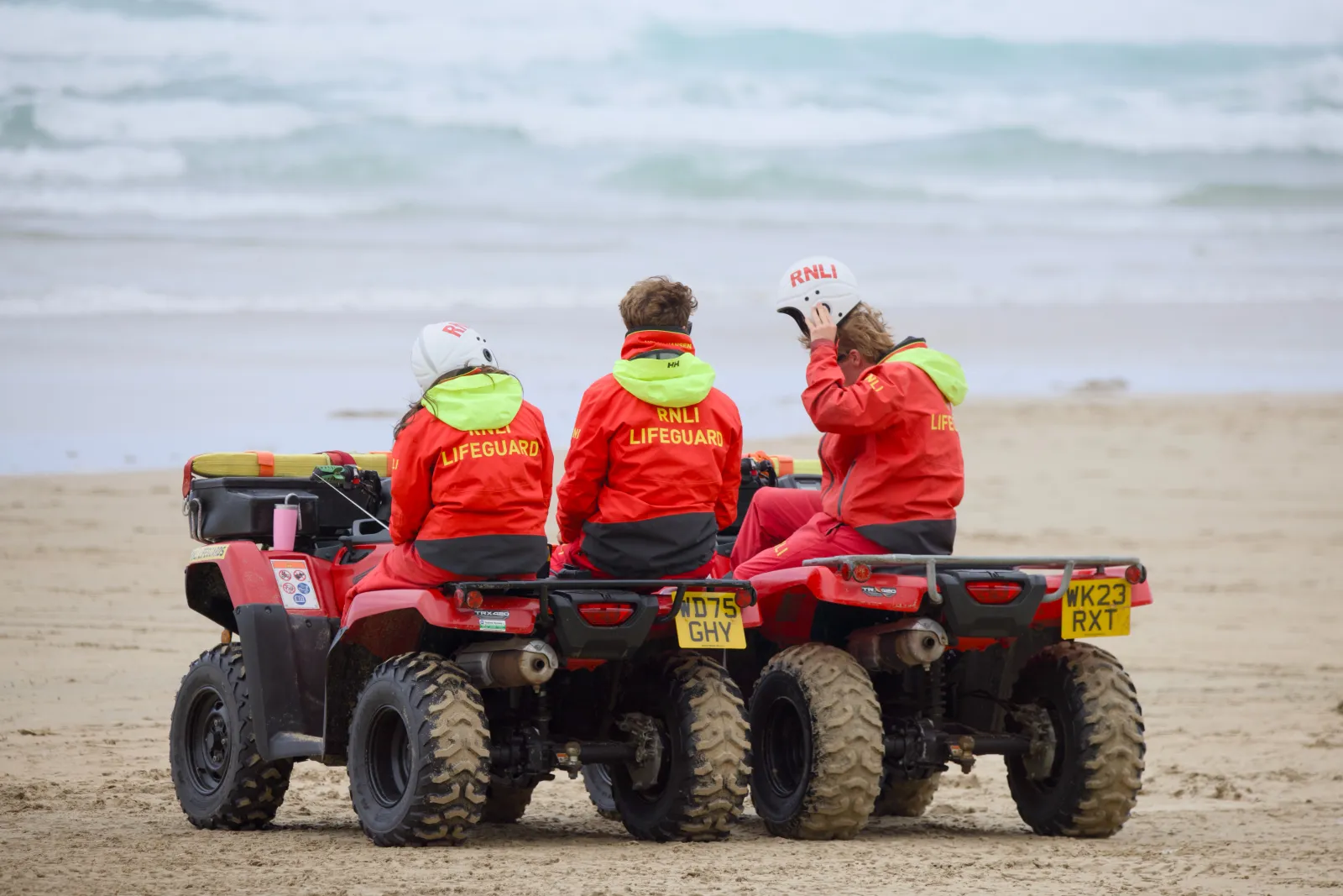 Three RNLI lifeguards on their quad bikes facing the sea