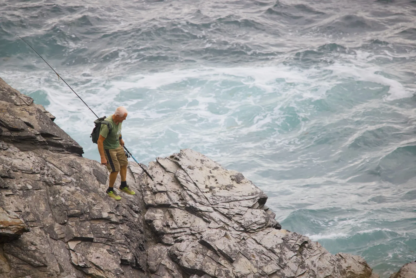 Angler with a fishing rod on the rocks above the sea
