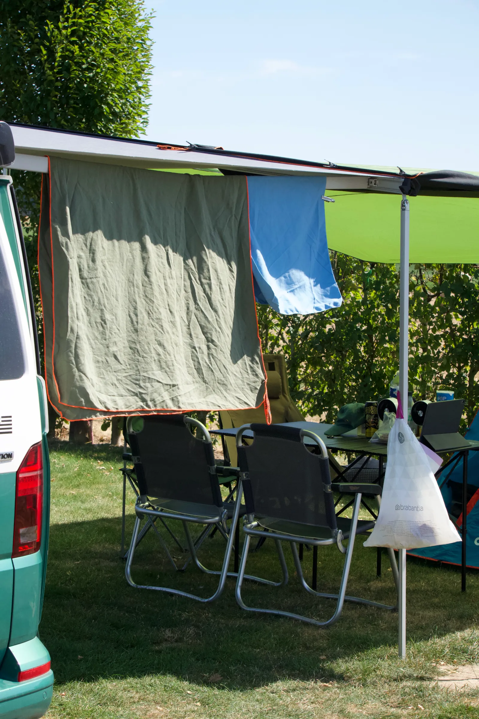 California with the awning out on a hedged pitch, towels drying