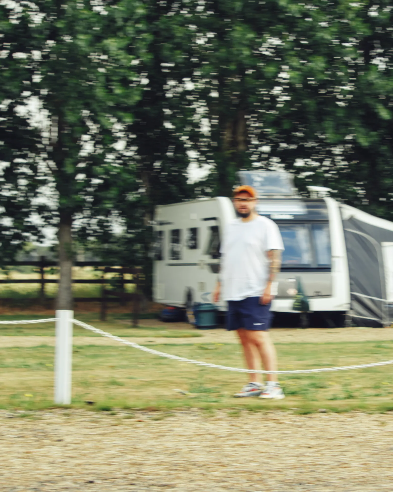 Sven at the rope fence of the pitch, slightly out of focus, a caravan behind