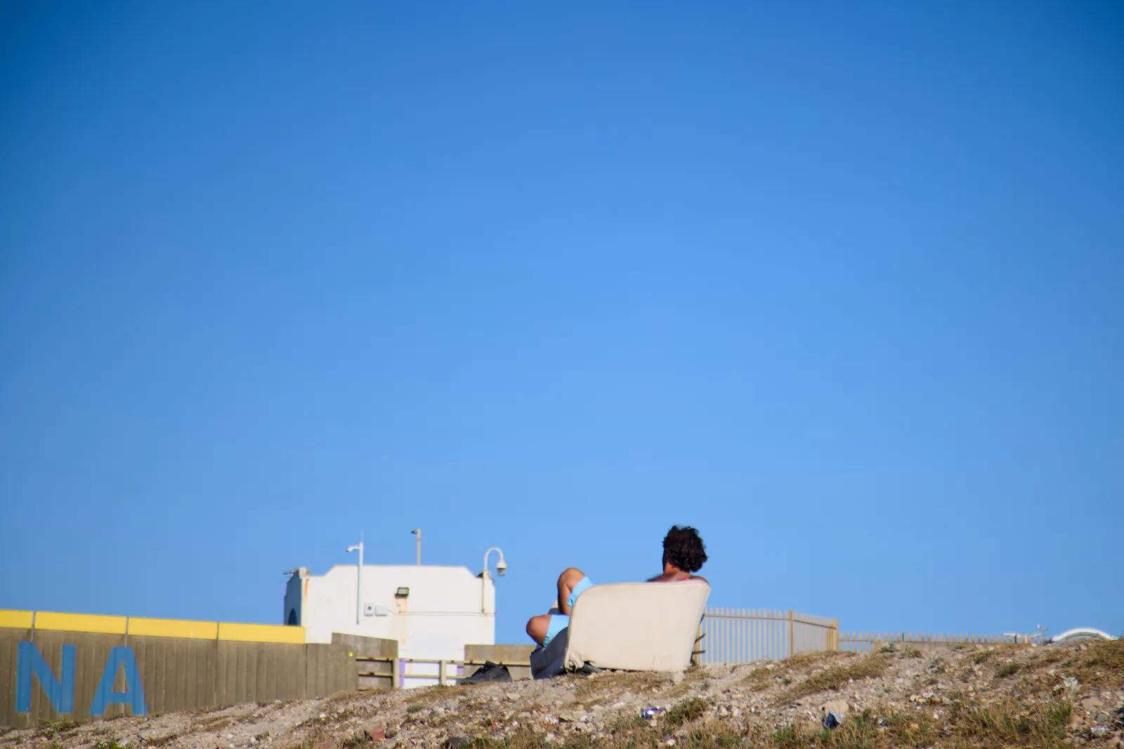 Man relaxing in an armchair on the shingle bank above the marina