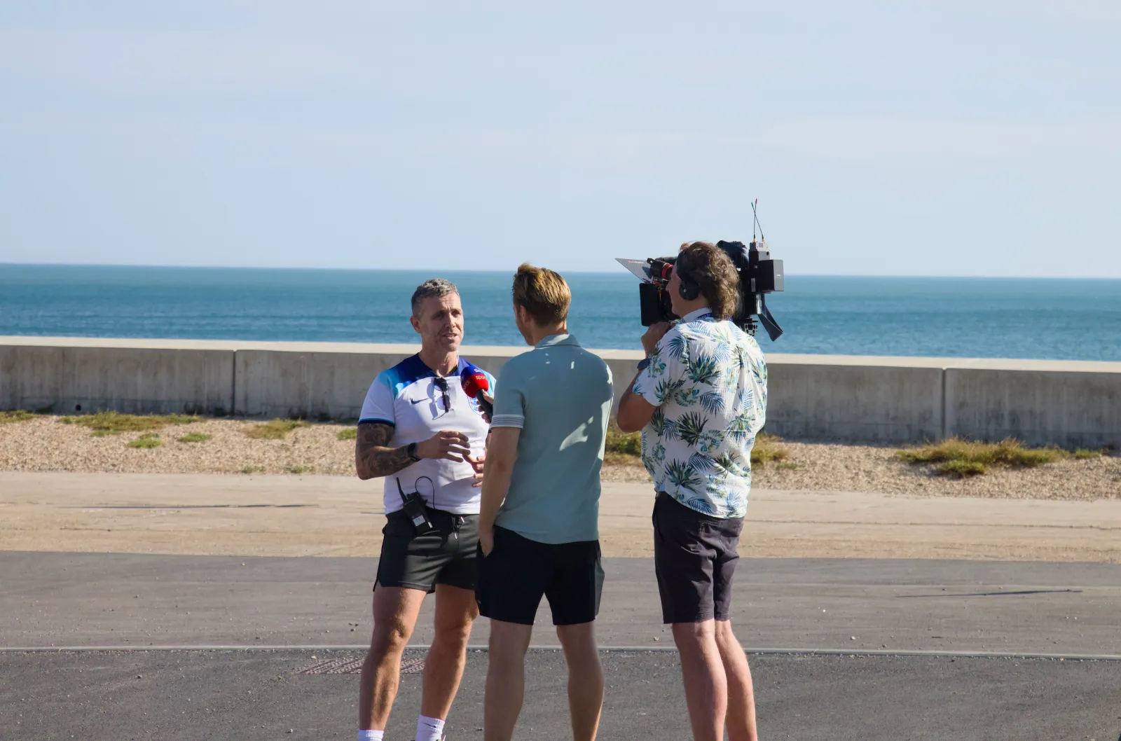 TV crew interviewing a man in an England shirt on the seafront