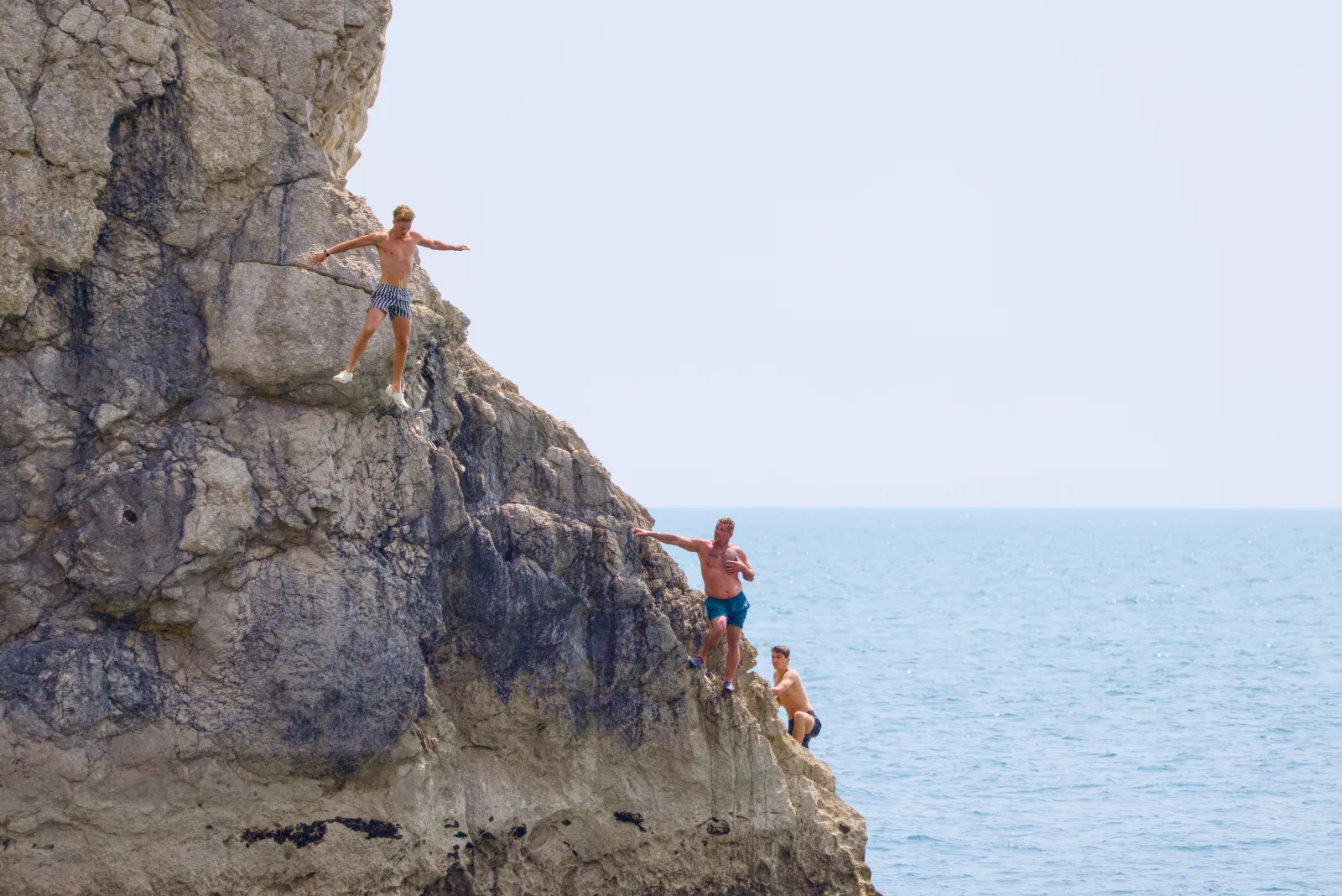 Three men climbing the rocks by the sea