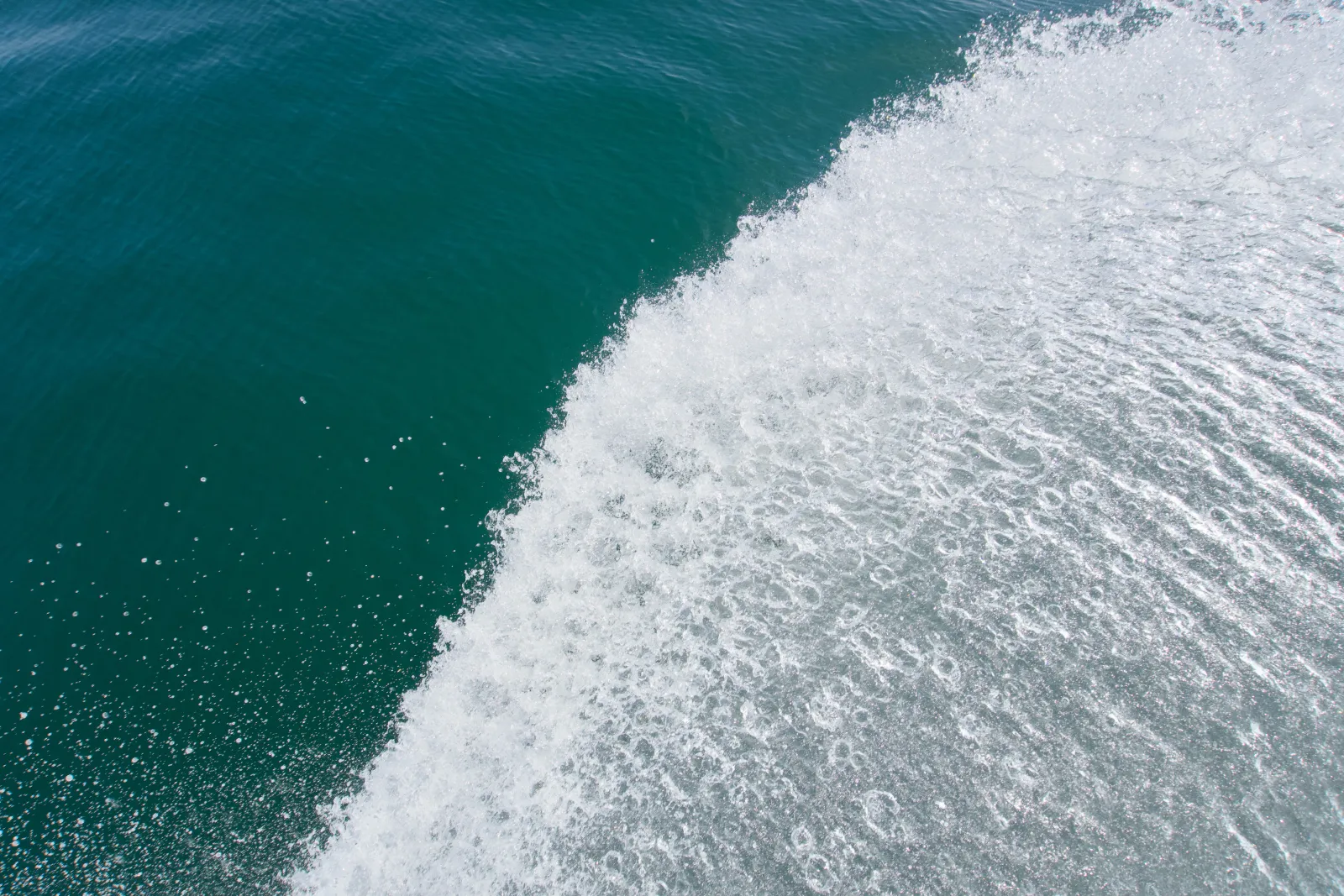 Top-down view of a boat's wake, white foam splitting against deep blue-green seawater