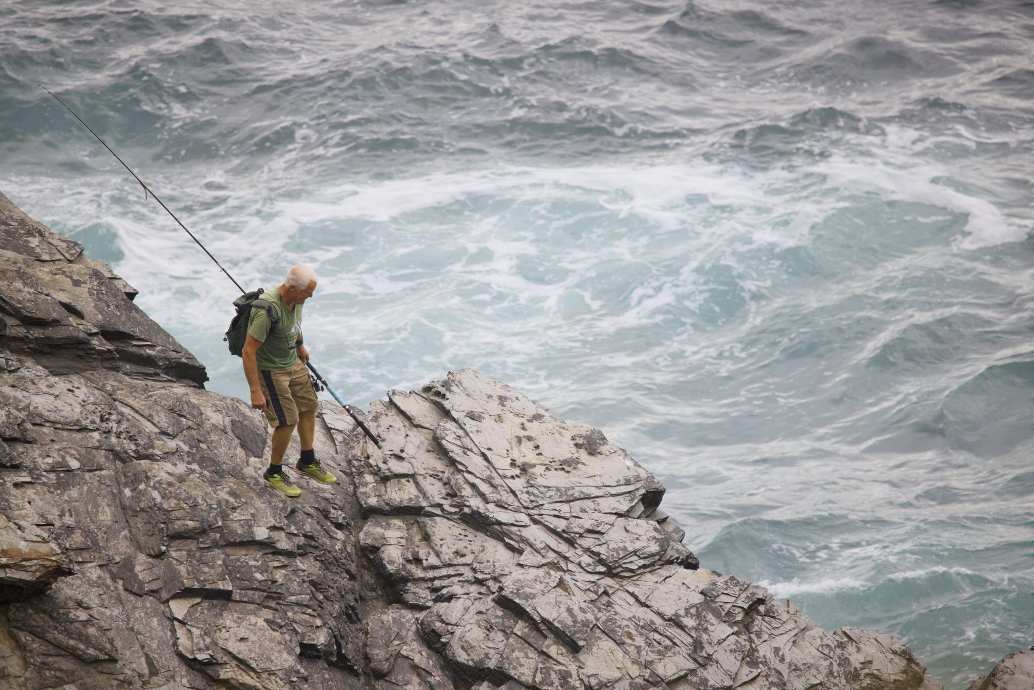 Angler with a fishing rod on the rocks above the sea