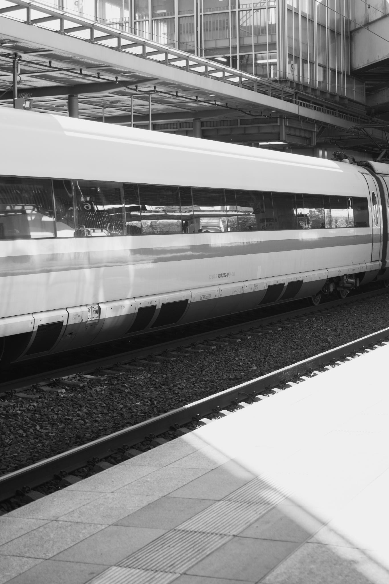 Black and white photograph of a Deutsche Bahn ICE high-speed train standing at a covered platform, clean side profile of a single carriage with the rails and a slice of light on the platform in the foreground