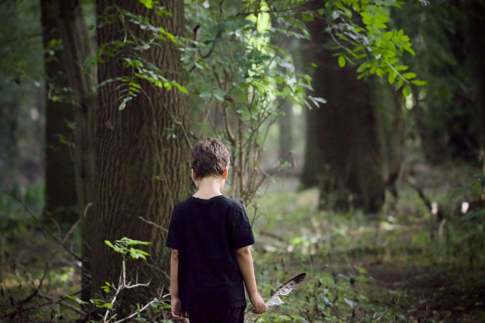 Tilian standing on a forest path, holding a feather