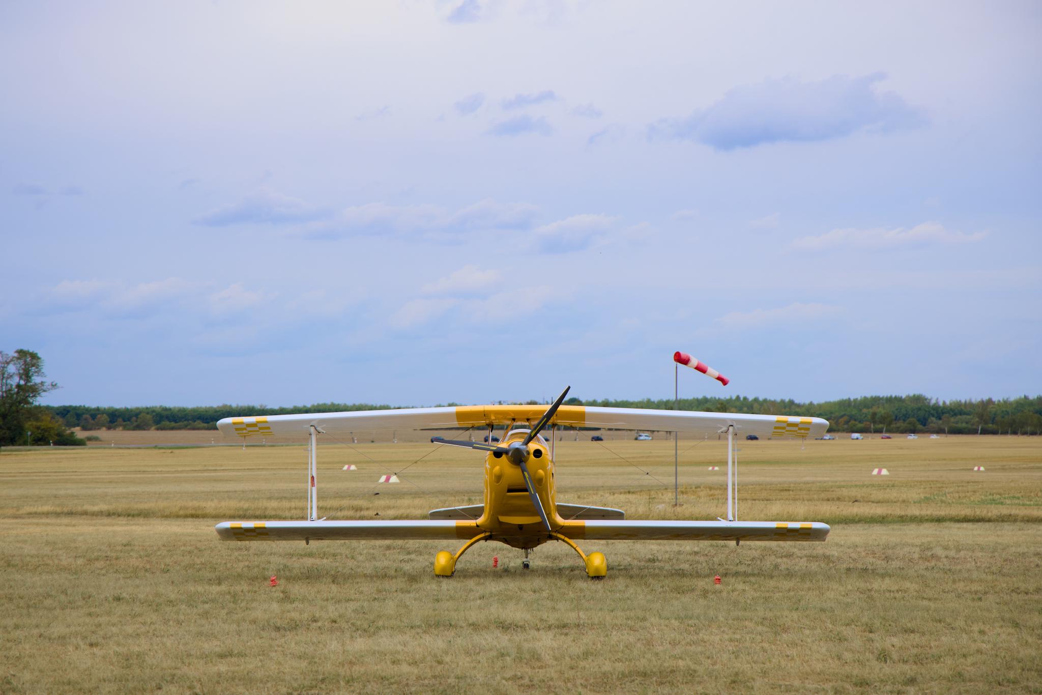 Yellow aerobatic biplane head-on with windsock
