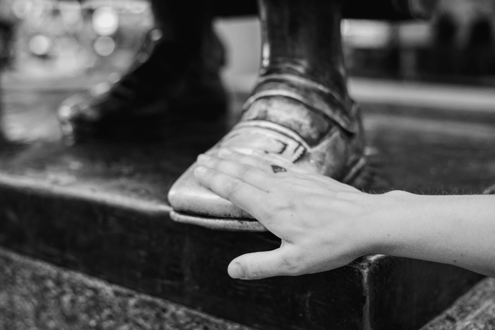 Black and white photo of a hand on the polished shoe of a bronze statue