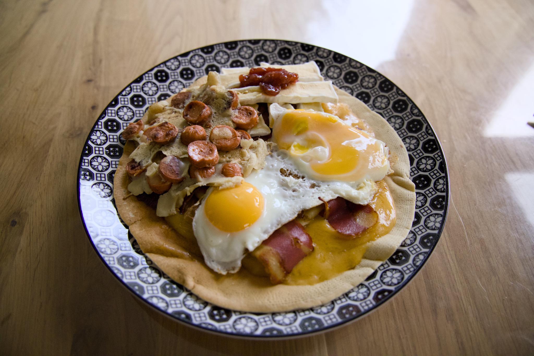 Double-layer pancake with fried eggs, vegan bacon, vegan sausage slices and strawberry jam