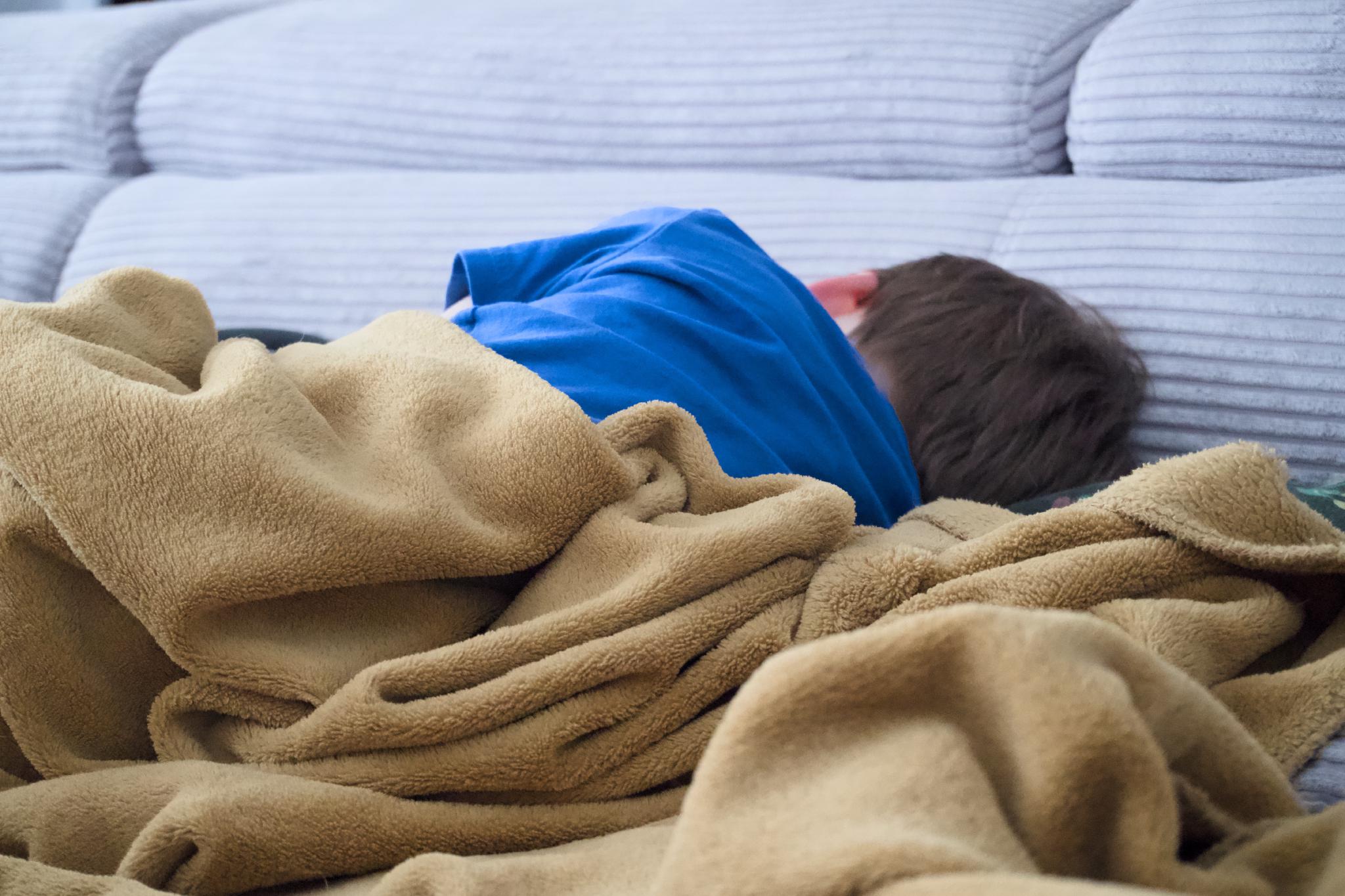 Child asleep on a couch wrapped in a blanket