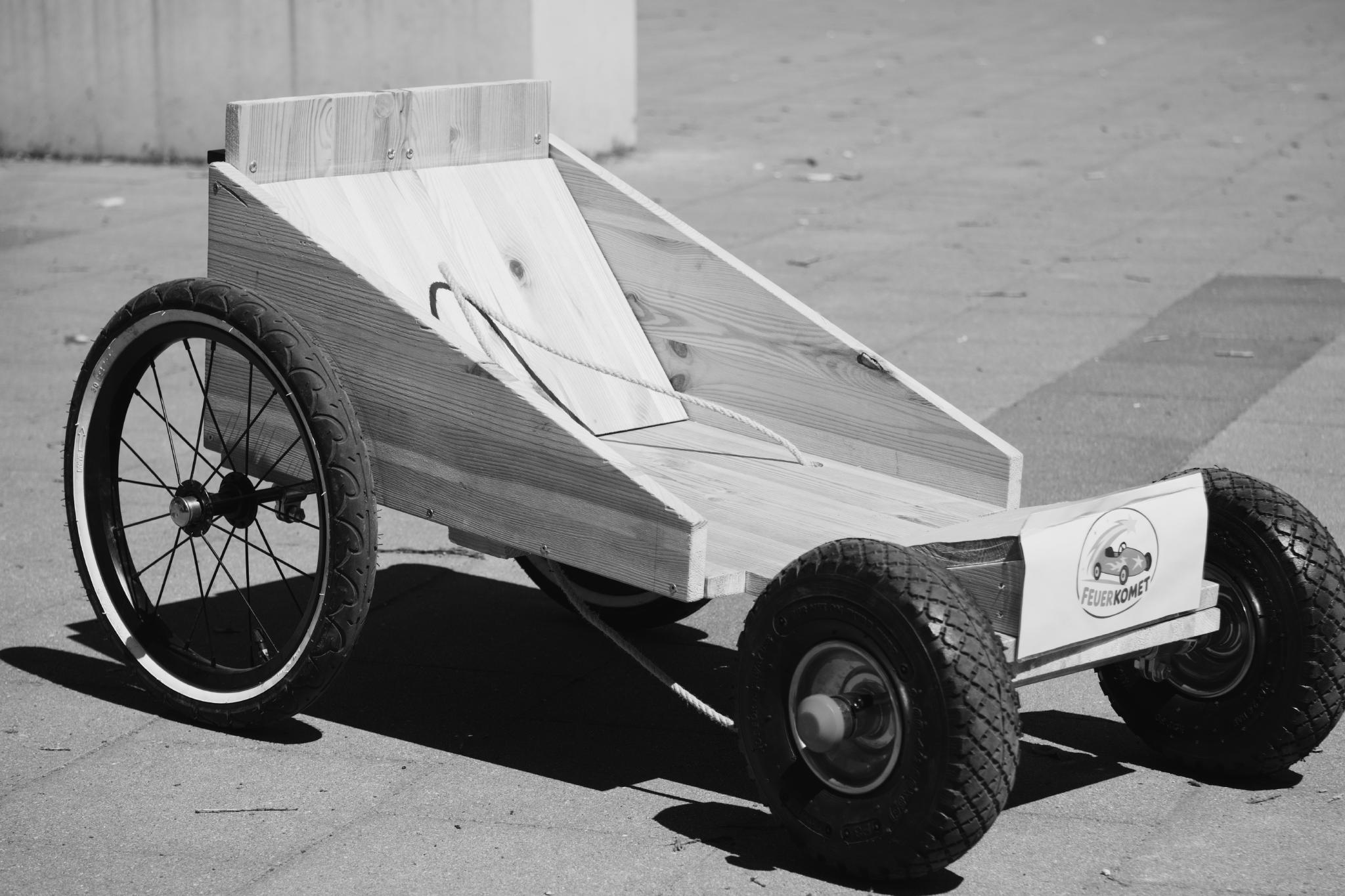 Black and white photo of a wooden soapbox cart with bicycle wheels on paving