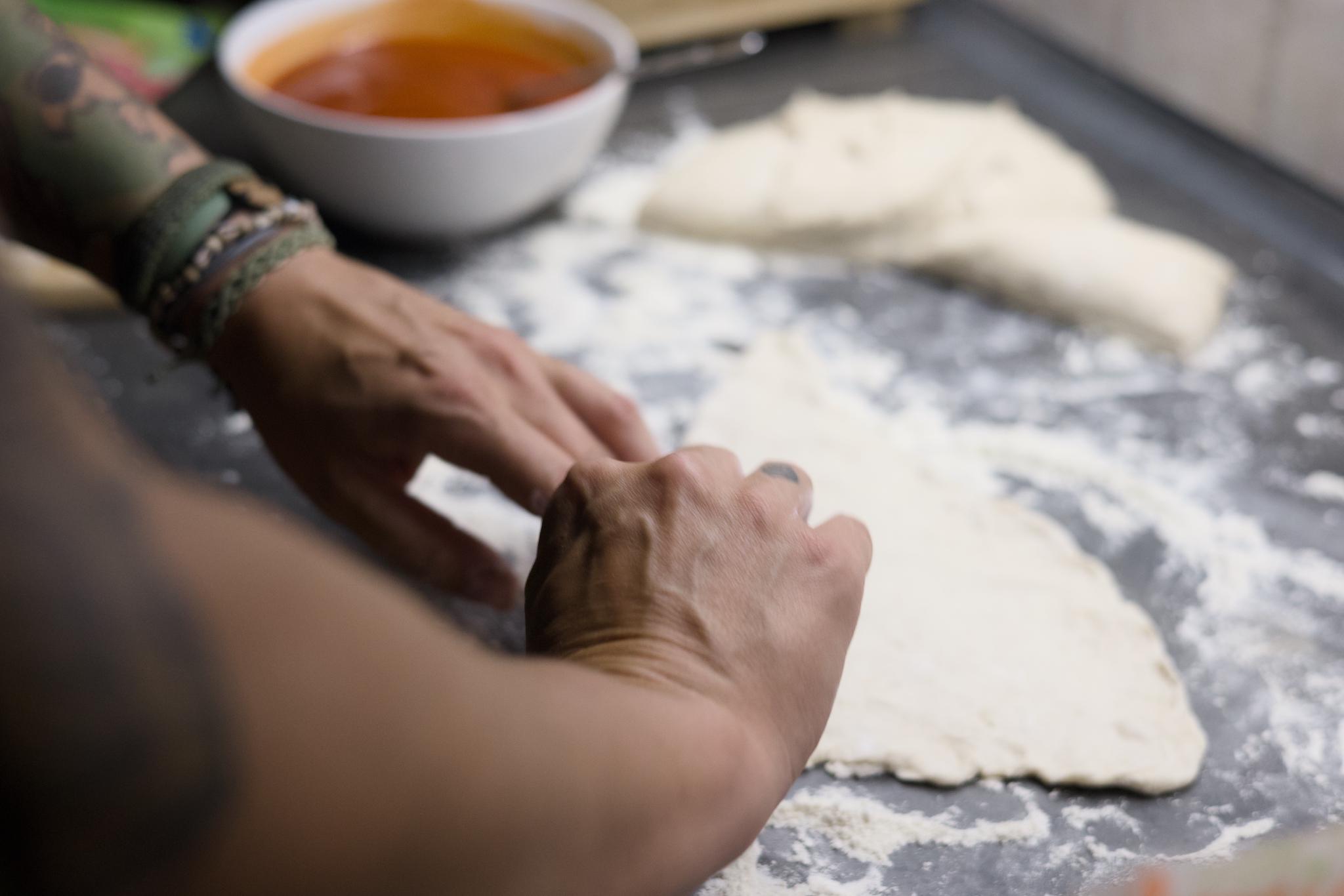 Nadine shaping pizza dough next to a bowl of tomato sauce