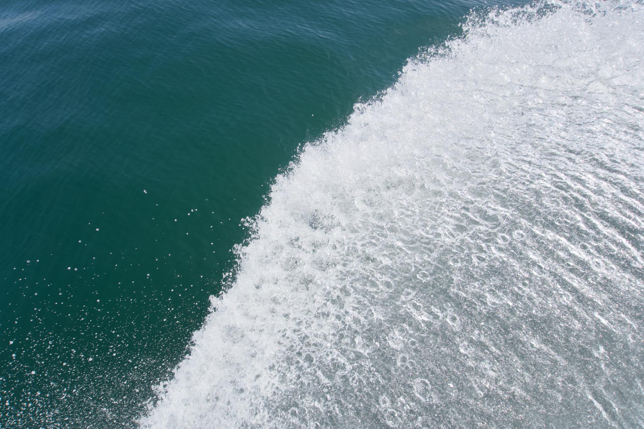 Top-down view of a boat's wake, white foam splitting against deep blue-green seawater
