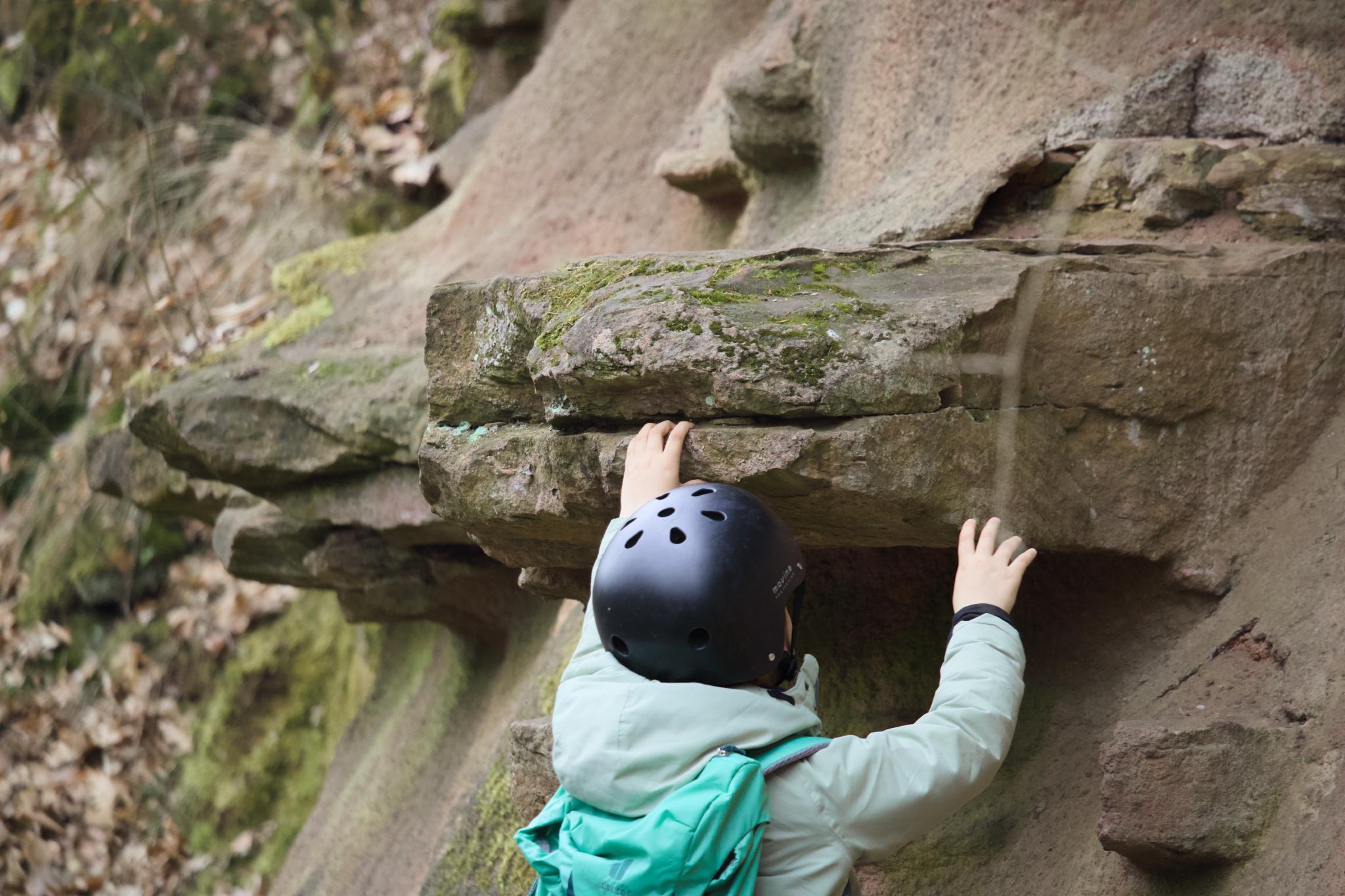 Child in green jacket reaching up to touch a sandstone rock face